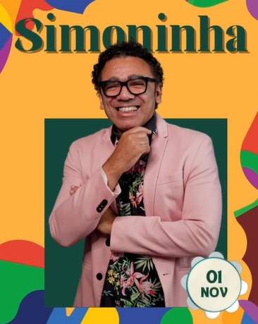 Imagem promocional do cantor Simoninha. Ele aparece sorrindo, usando um blazer rosa claro sobre uma camisa floral escura, com os braços cruzados. O fundo é composto de cores vibrantes, com detalhes gráficos em formas abstratas em tons de verde, laranja, roxo e azul. Na parte superior, está escrito "Simoninha" em letras grandes e verdes, e na parte inferior direita, há um selo com a data "01 NOV", indicando o dia da apresentação.