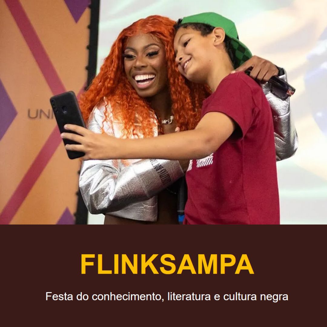 Mulher negra de cabelos ruivos e blusa metálica sorri enquanto tira uma selfie com um menino de boné verde e camiseta vermelha. Ambos estão abraçados e felizes em um ambiente colorido, com o logotipo da Universidade Zumbi dos Palmares ao fundo. Fim da descrição.